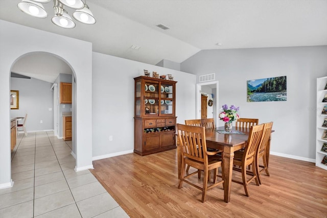 dining room with light wood-style floors, vaulted ceiling, visible vents, and arched walkways