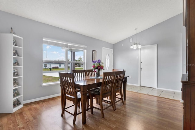 dining room with lofted ceiling, a textured ceiling, an inviting chandelier, light wood finished floors, and baseboards