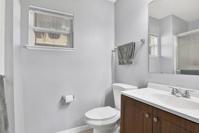 bathroom featuring a stall shower, toilet, vanity, and baseboards