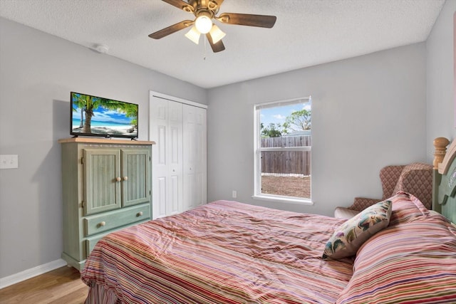 bedroom with light wood finished floors, baseboards, ceiling fan, a closet, and a textured ceiling