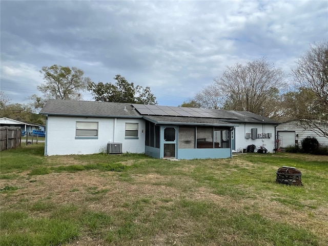 rear view of house with an outdoor fire pit, concrete block siding, a lawn, and a sunroom