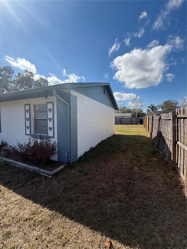 view of home's exterior with concrete block siding, a lawn, and a fenced backyard