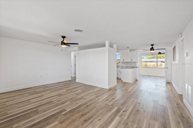 unfurnished living room featuring light wood-style flooring, a ceiling fan, visible vents, and baseboards