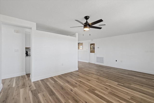 spare room with visible vents, brick wall, wood finished floors, and a ceiling fan