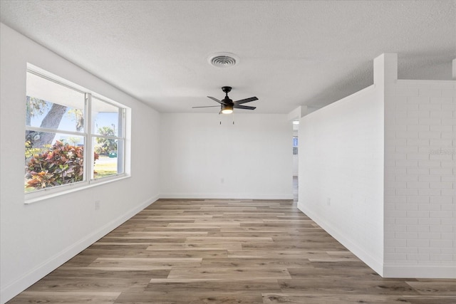 empty room with visible vents, a ceiling fan, a textured ceiling, wood finished floors, and baseboards