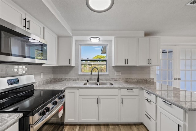 kitchen with a peninsula, a sink, stainless steel appliances, white cabinets, and light wood-style floors