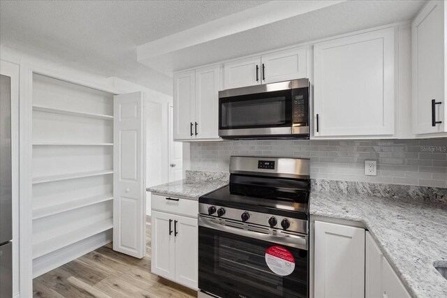 kitchen featuring white cabinetry, decorative backsplash, light wood-type flooring, and appliances with stainless steel finishes