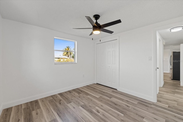 unfurnished bedroom featuring light wood-type flooring, baseboards, and freestanding refrigerator