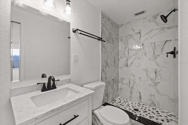 full bathroom featuring vanity, a shower stall, toilet, and a textured wall