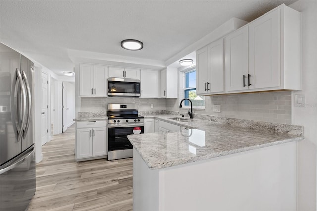 10841 Scenic Dr, Port Richey, FL 34668 - kitchen with stainless steel appliances, light wood-style flooring, white cabinets, and a peninsula