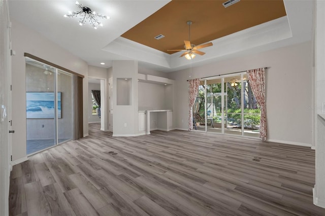 unfurnished living room featuring visible vents, ceiling fan with notable chandelier, wood finished floors, baseboards, and a raised ceiling