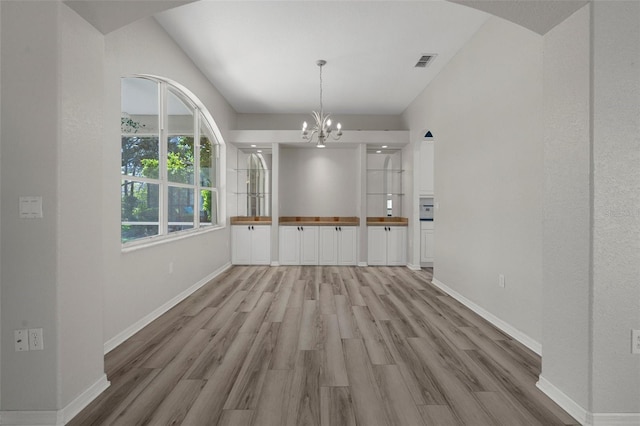 unfurnished dining area featuring visible vents, baseboards, light wood-style floors, and a notable chandelier