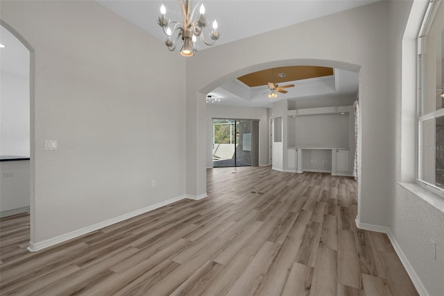 interior space featuring light wood-style flooring, a ceiling fan, a tray ceiling, arched walkways, and baseboards