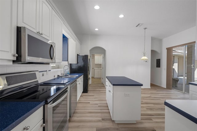 kitchen with a center island, stainless steel appliances, arched walkways, white cabinetry, and a sink