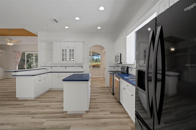 kitchen featuring a healthy amount of sunlight, a peninsula, stainless steel appliances, arched walkways, and white cabinetry