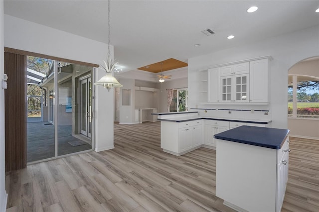 kitchen featuring arched walkways, visible vents, white cabinetry, and light wood-type flooring