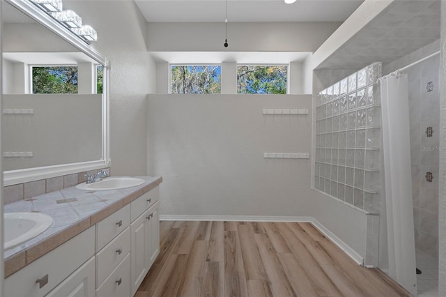 full bath with a sink, wood finished floors, double vanity, and a tile shower