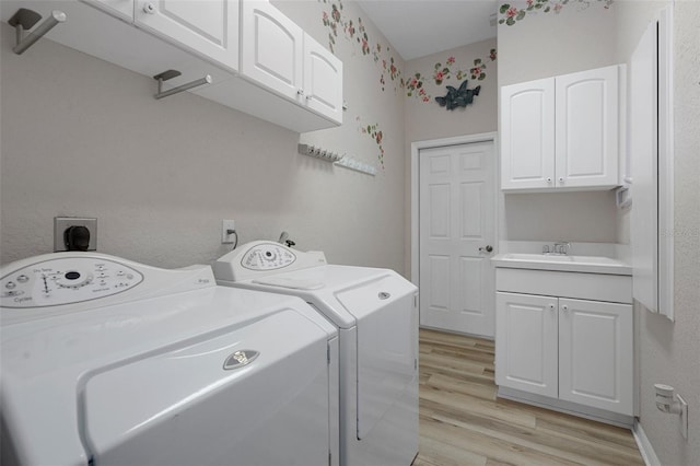 clothes washing area with cabinet space, washing machine and dryer, light wood-style flooring, and a sink