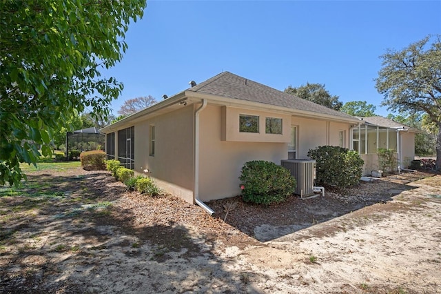 view of side of property featuring central air condition unit, stucco siding, a shingled roof, and glass enclosure