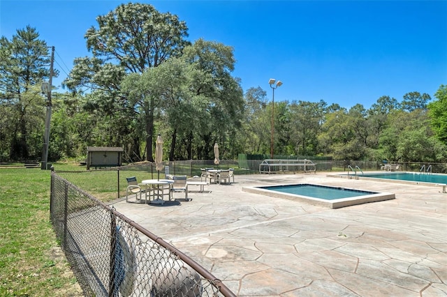 pool with a patio, a lawn, and fence