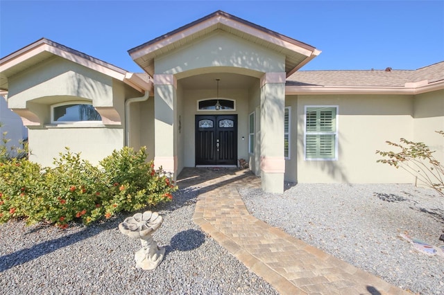 entrance to property with a shingled roof and stucco siding