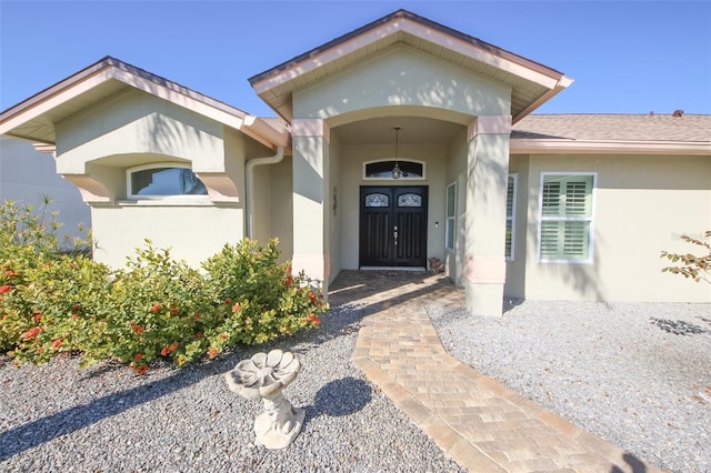 doorway to property featuring stucco siding and a shingled roof