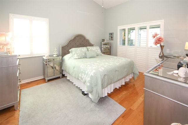 bedroom with lofted ceiling, light wood-style floors, and baseboards