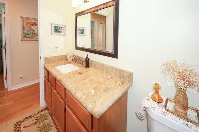 half bathroom featuring baseboards, toilet, wood finished floors, and vanity