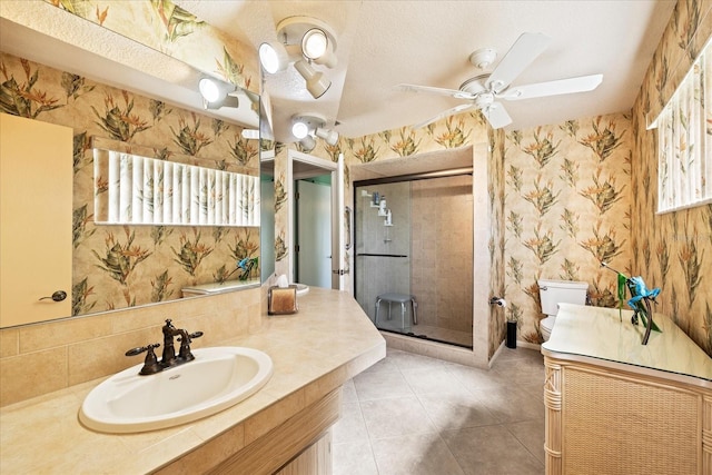 bathroom with vanity, a ceiling fan, wallpapered walls, a shower stall, and toilet