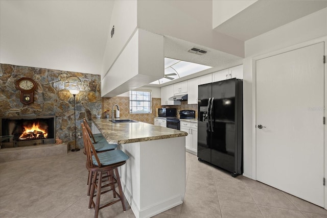 kitchen featuring under cabinet range hood, a peninsula, a kitchen breakfast bar, black appliances, and a sink