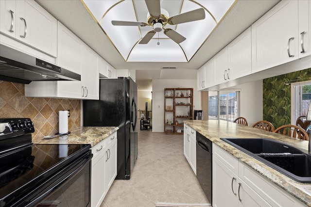 kitchen with ceiling fan, under cabinet range hood, a tray ceiling, white cabinets, and black appliances