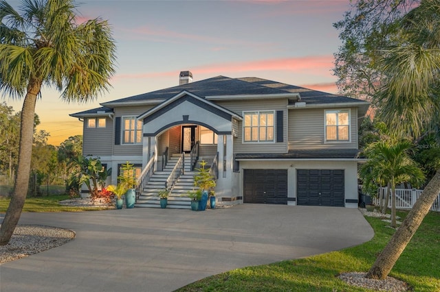 beach home with fence, concrete driveway, stairs, a chimney, and an attached garage