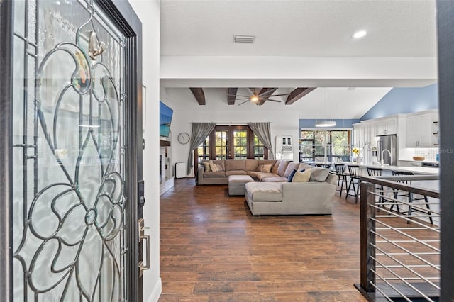 foyer entrance featuring dark wood-type flooring, lofted ceiling with beams, visible vents, and a textured ceiling