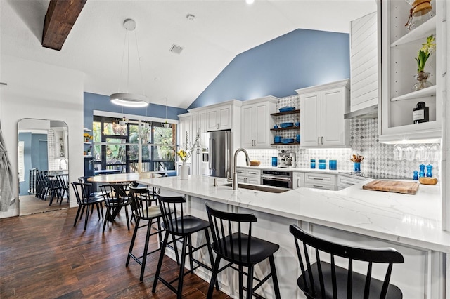 kitchen with a sink, stainless steel appliances, arched walkways, decorative backsplash, and dark wood-style flooring