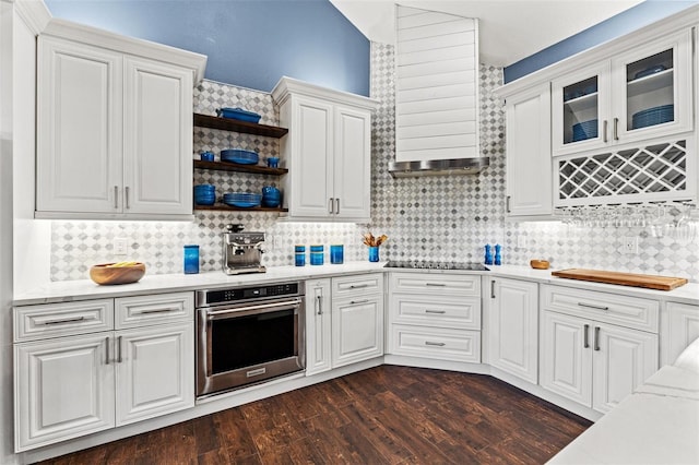 kitchen featuring oven, black electric stovetop, dark wood finished floors, decorative backsplash, and white cabinetry