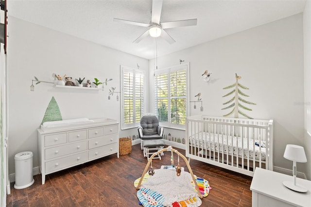 bedroom with a crib, wood finished floors, baseboards, and ceiling fan