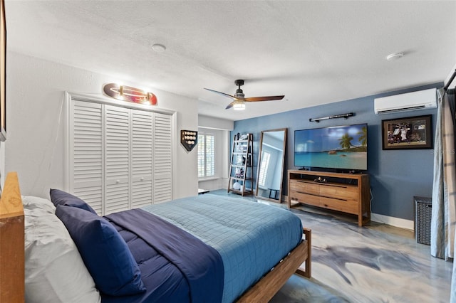 bedroom with an AC wall unit, a textured ceiling, finished concrete floors, a closet, and baseboards