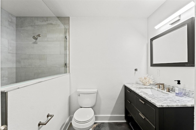 bathroom featuring baseboards, toilet, a tile shower, wood finished floors, and vanity