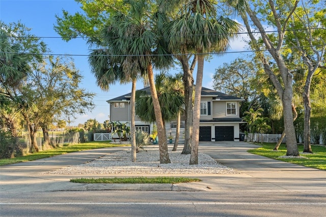 coastal home with concrete driveway, an attached garage, and fence