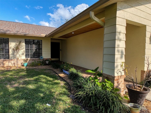 property entrance featuring a lawn and a shingled roof