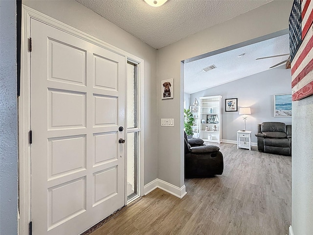 entrance foyer featuring visible vents, baseboards, vaulted ceiling, wood finished floors, and a textured ceiling