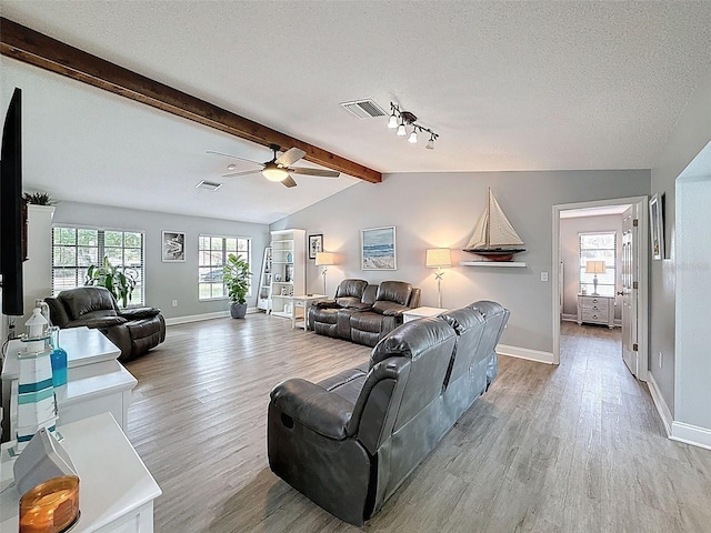 living area with visible vents, light wood-style flooring, a textured ceiling, and vaulted ceiling with beams