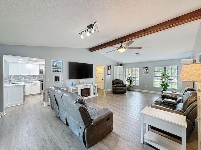 living area featuring vaulted ceiling with beams, light wood-type flooring, and a textured ceiling