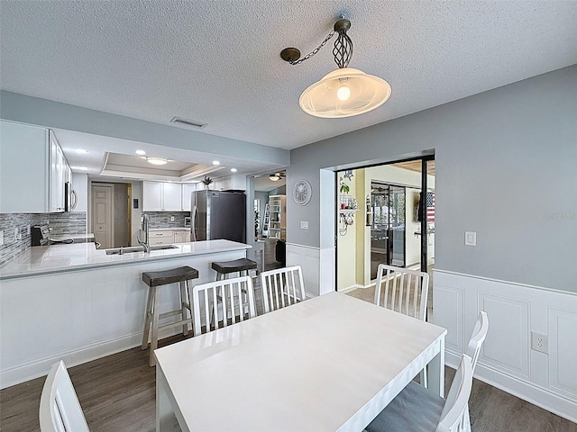 dining area with visible vents, a textured ceiling, a wainscoted wall, and dark wood-style flooring