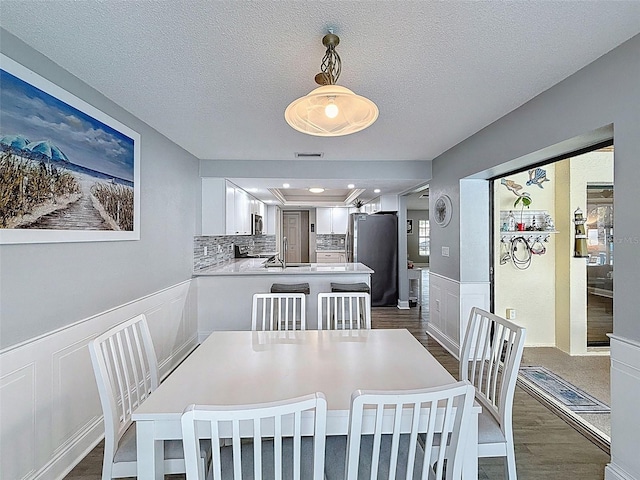 dining area with dark wood-style floors, visible vents, a wainscoted wall, a textured ceiling, and a decorative wall