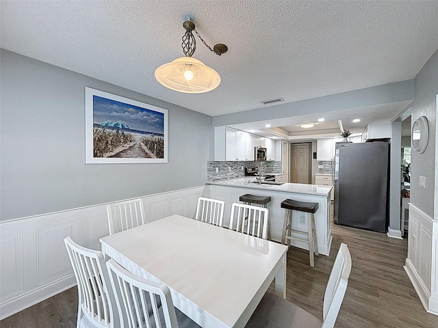 dining area featuring dark wood finished floors, visible vents, wainscoting, and a textured ceiling