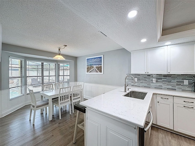 kitchen featuring a peninsula, white cabinets, wood finished floors, and a sink