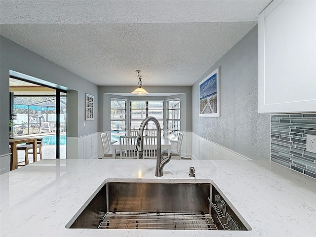 kitchen with a sink, a wainscoted wall, light stone counters, and a textured ceiling