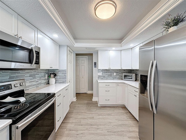 kitchen featuring a tray ceiling, light countertops, light wood-style floors, appliances with stainless steel finishes, and white cabinetry