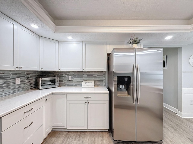 kitchen with backsplash, stainless steel fridge with ice dispenser, a toaster, light wood-style flooring, and white cabinets